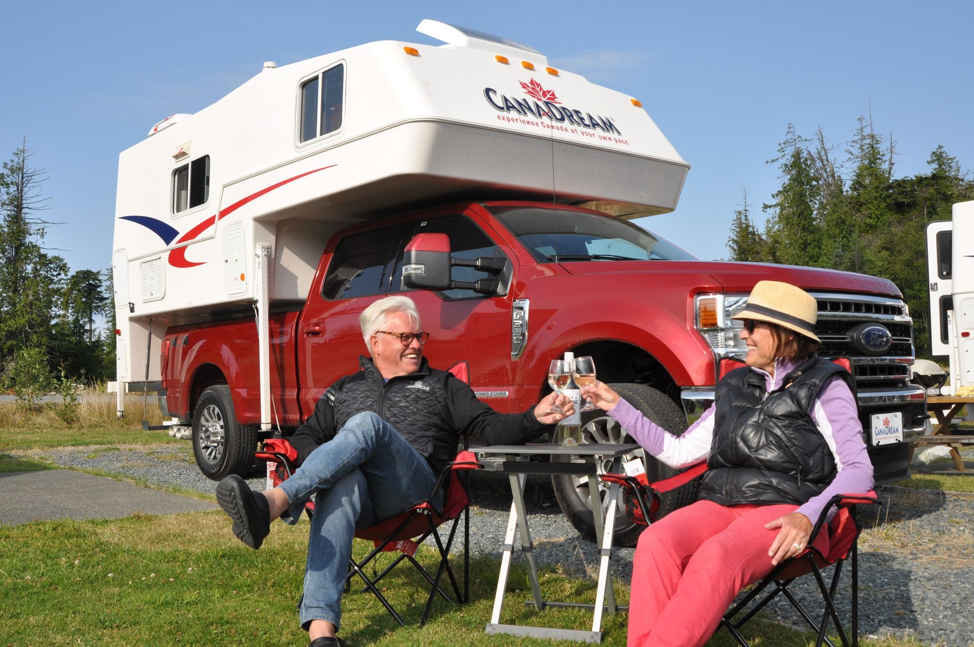 Twee mensen ontspannen naast een rode Maxi Travel 4x4 Camper op een zonnige plek