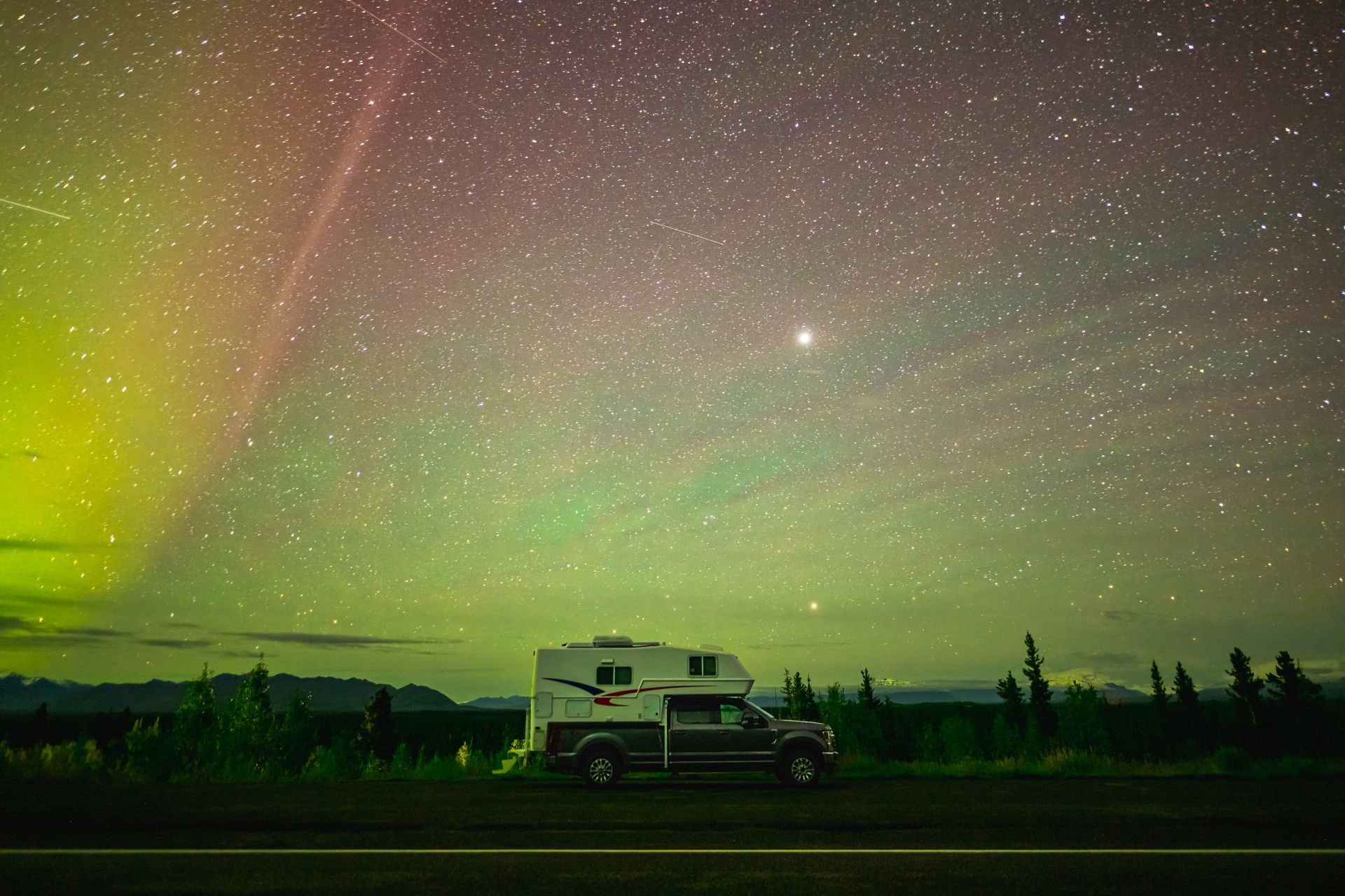 Maxi Travel 4x4 Camper geparkeerd onder een sterrenhemel met groen en roze noorderlicht