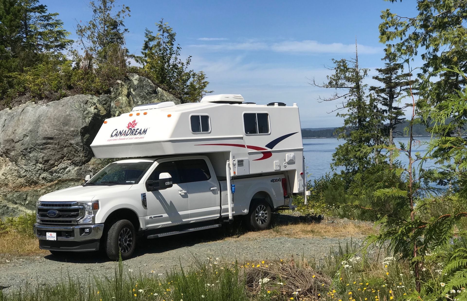 Maxi Travel 4x4 Camper langs een meer, met bomen en een rotsachtige oever