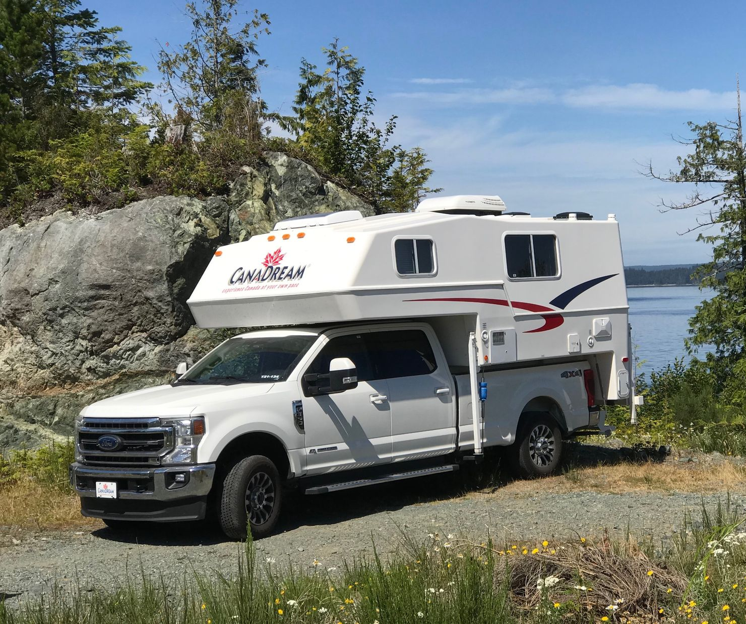 Maxi Travel 4x4 Camper geparkeerd aan een rotsachtige oever van een meer onder een blauwe hemel
