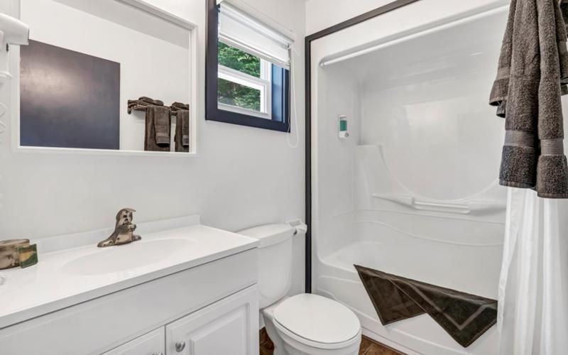 Lichte, witte badkamer met wastafel, spiegel, raam en betegelde douche met handdoekhouder in de buurt.