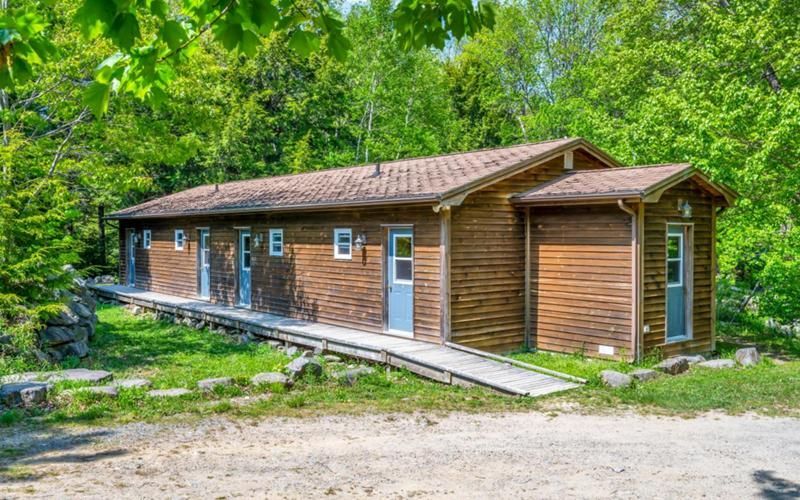 Houten blokhut met blauwe deuren en een hellingbaan, gelegen in een groen bosrijk gebied.