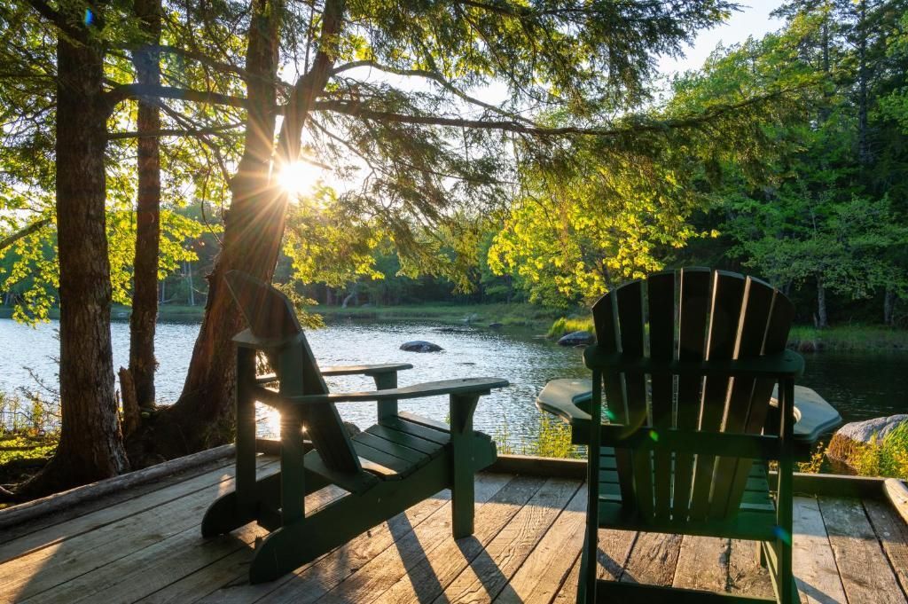 Zonnig terras aan het meer met twee Adirondack-stoelen, gericht op het water bij zonsondergang.