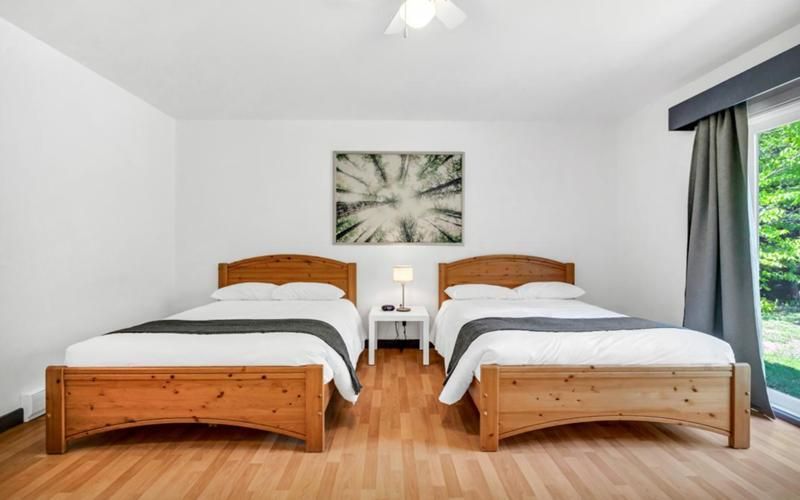 Lichte slaapkamer met twee eenpersoonsbedden, witte muren, houten vloer en een raam met uitzicht op groen.