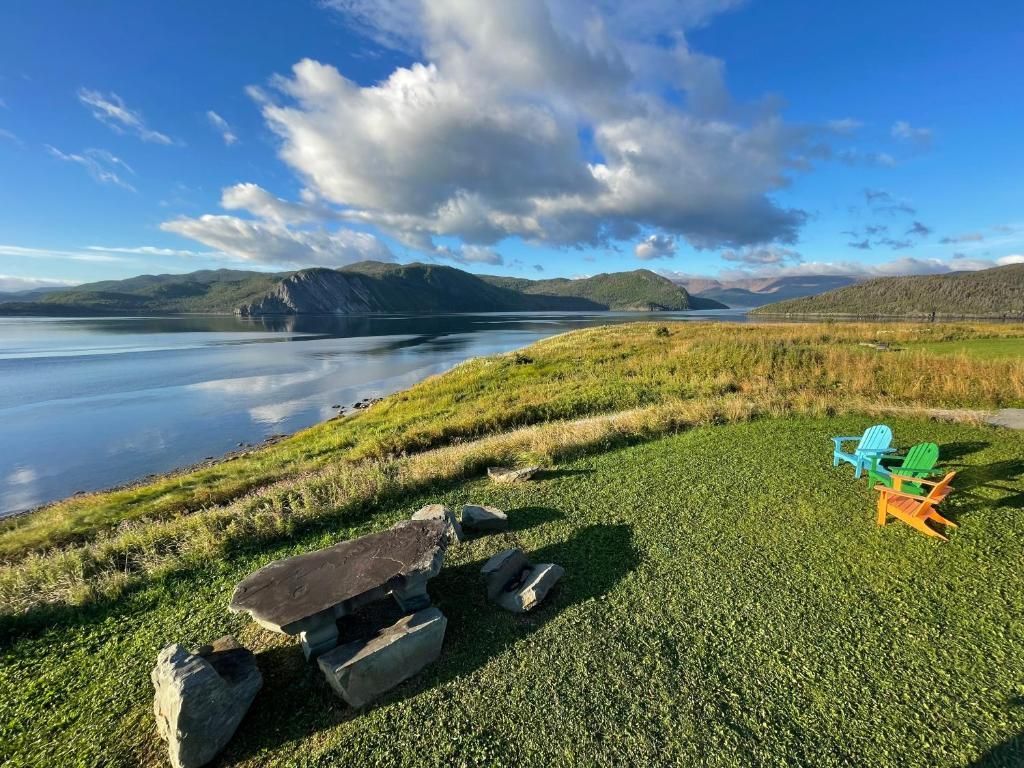 Een meer en heuvels onder een bewolkte blauwe hemel, met een picknicktafel en kleurrijke stoelen op een grasveldje met uitzicht.