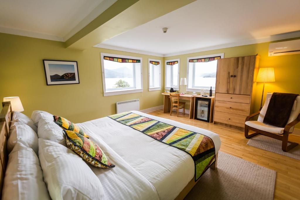 Een felgele slaapkamer met een wit bed, een kleurrijke sprei, ramen, een houten kledingkast en fauteuils.