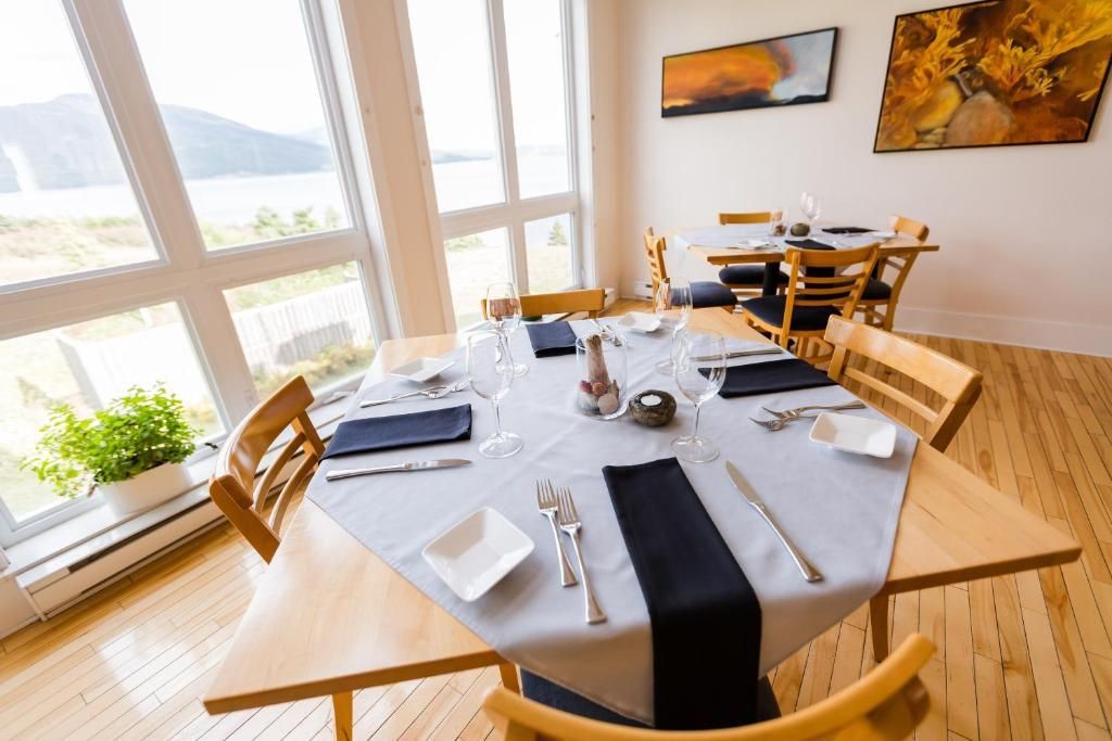 Lichte eetkamer met een gedekte tafel, houten stoelen, grote ramen en uitzicht op het landschap.