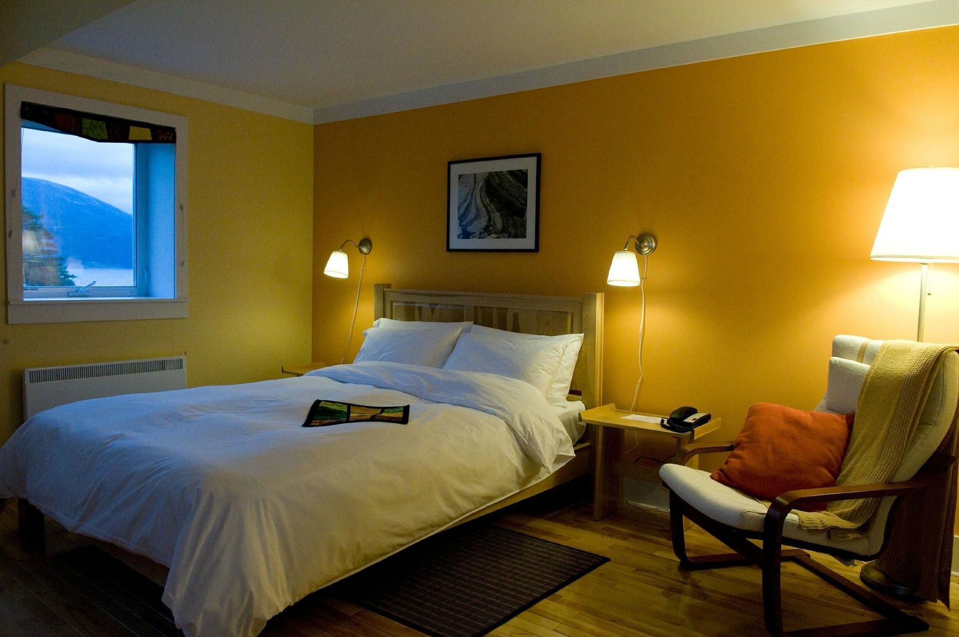 Gezellige hotelkamer met een bed, lampen, stoel, gele muren en een raam met uitzicht op de bergen.