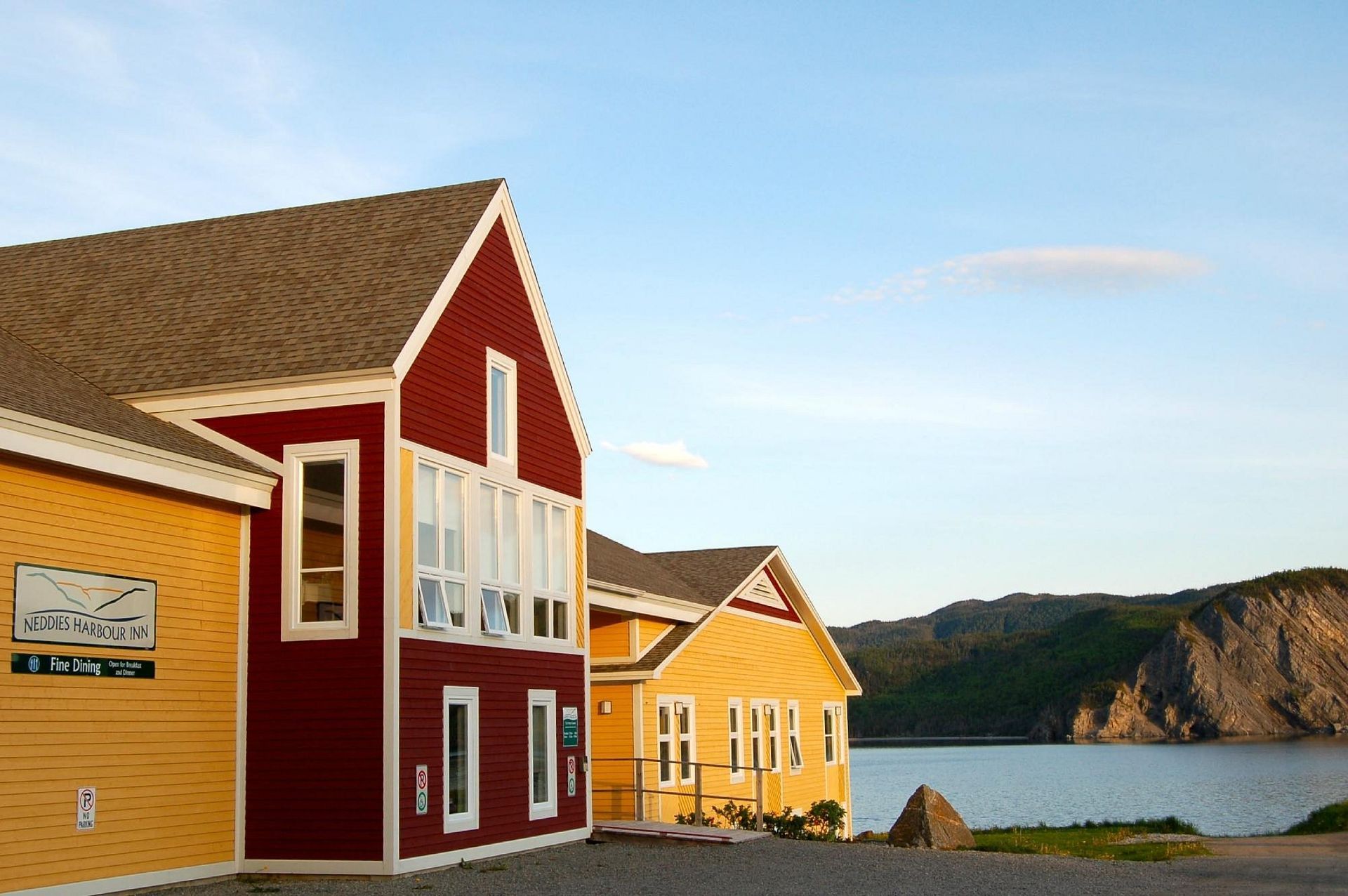Kleurrijke huisjes aan zee, aan het kalme water en met rotsachtige kliffen op de achtergrond bij zonsondergang.