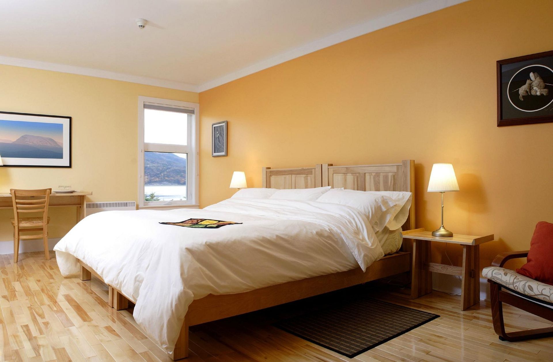 Ruime slaapkamer met een groot bed, warme gele muren, een houten vloer en een raam met uitzicht.