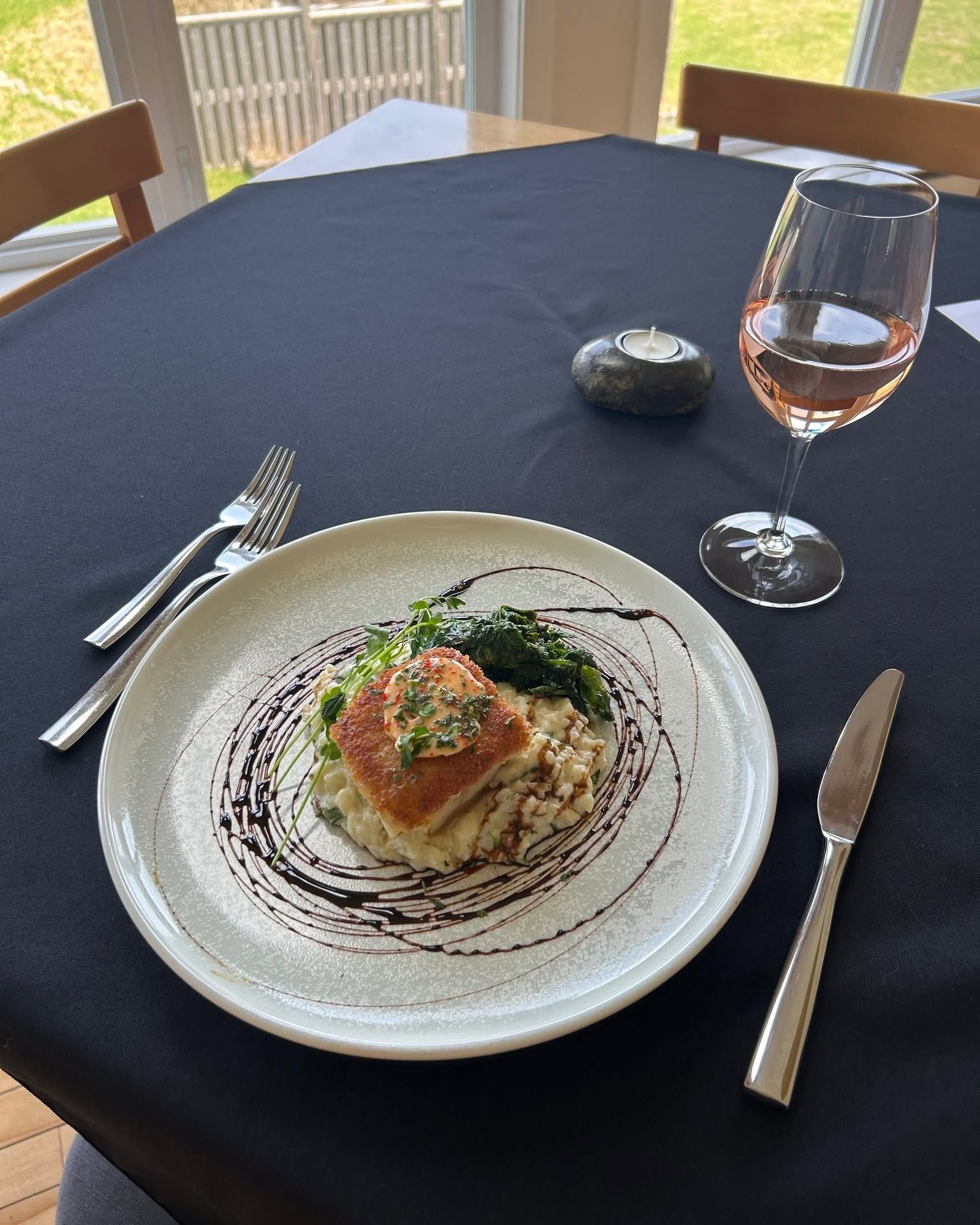 Restauranttafel met hoofdgerecht, wijnglas en bestek op een zwart tafelkleed.