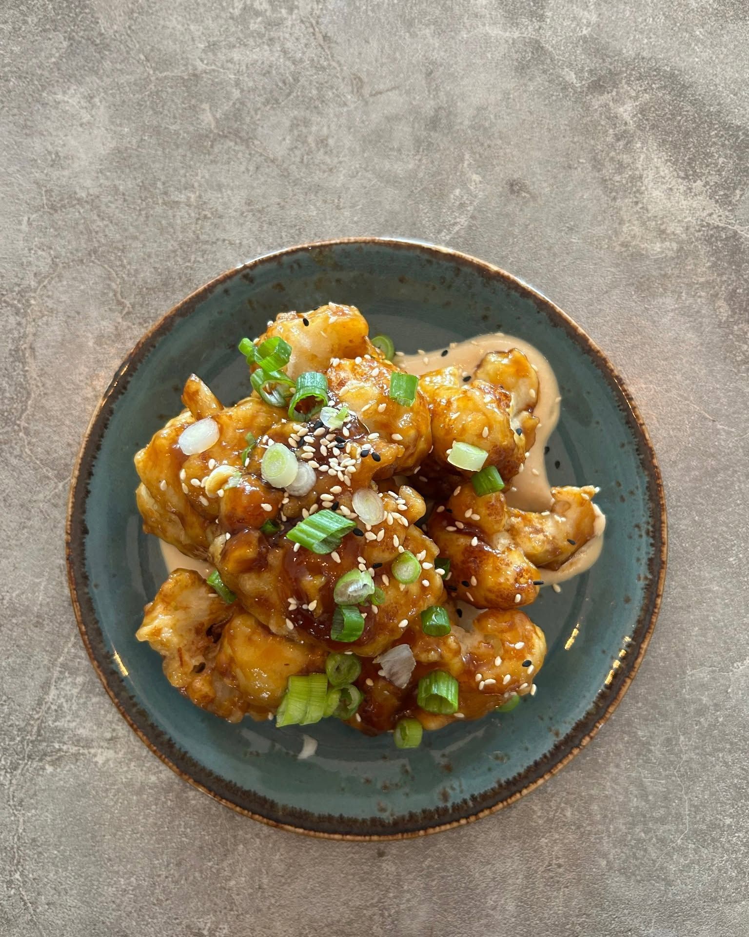 Dumplings in saus op een donker bord, gegarneerd met lente-uitjes en sesamzaadjes.