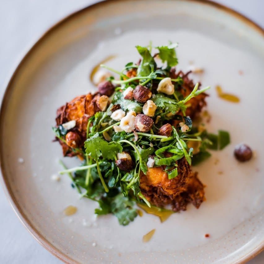 Een prachtig opgemaakt gastronomisch gerecht met groenten, kruiden, geroosterde stukjes en saus, geserveerd op een wit bord.
