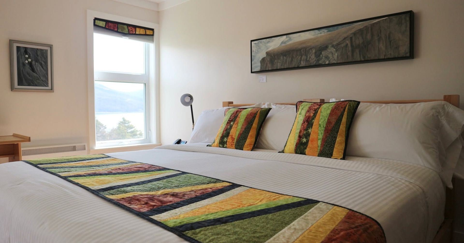 Netjes opgemaakt bed met kleurrijk gestreept beddengoed in een lichte slaapkamer bij een raam.