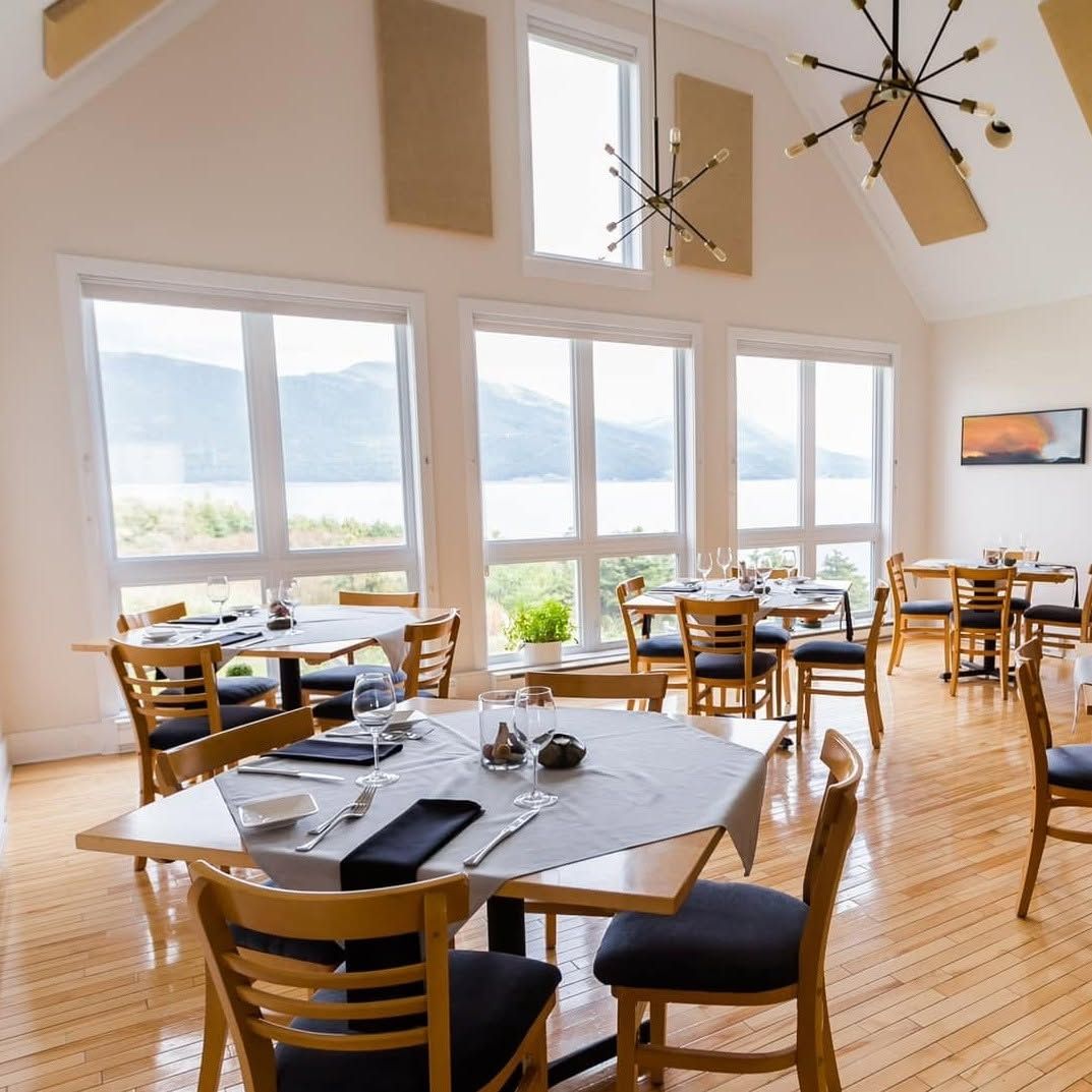 Licht restaurant aan het meer met grote ramen, houten tafels en hangende plafondventilatoren.