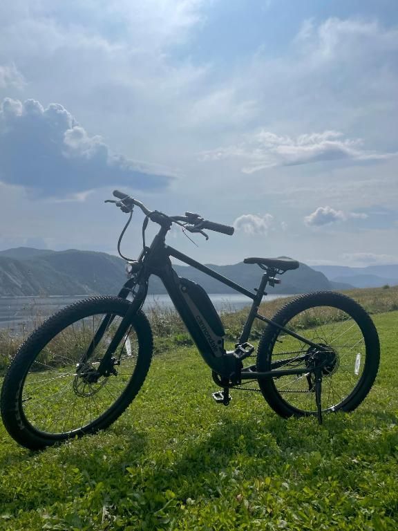 Zwarte elektrische fiets op een grasheuvel met bergen en een bewolkte hemel op de achtergrond.