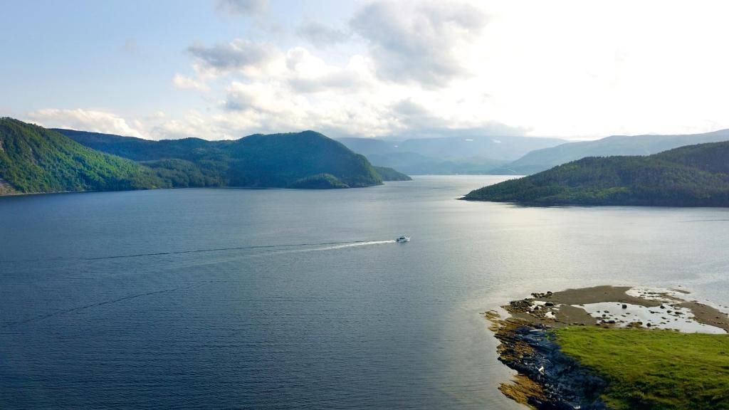 Een kalm blauw meer tussen groene bergen onder een bewolkte hemel, met een klein bootje dat een kielzog achterlaat.
