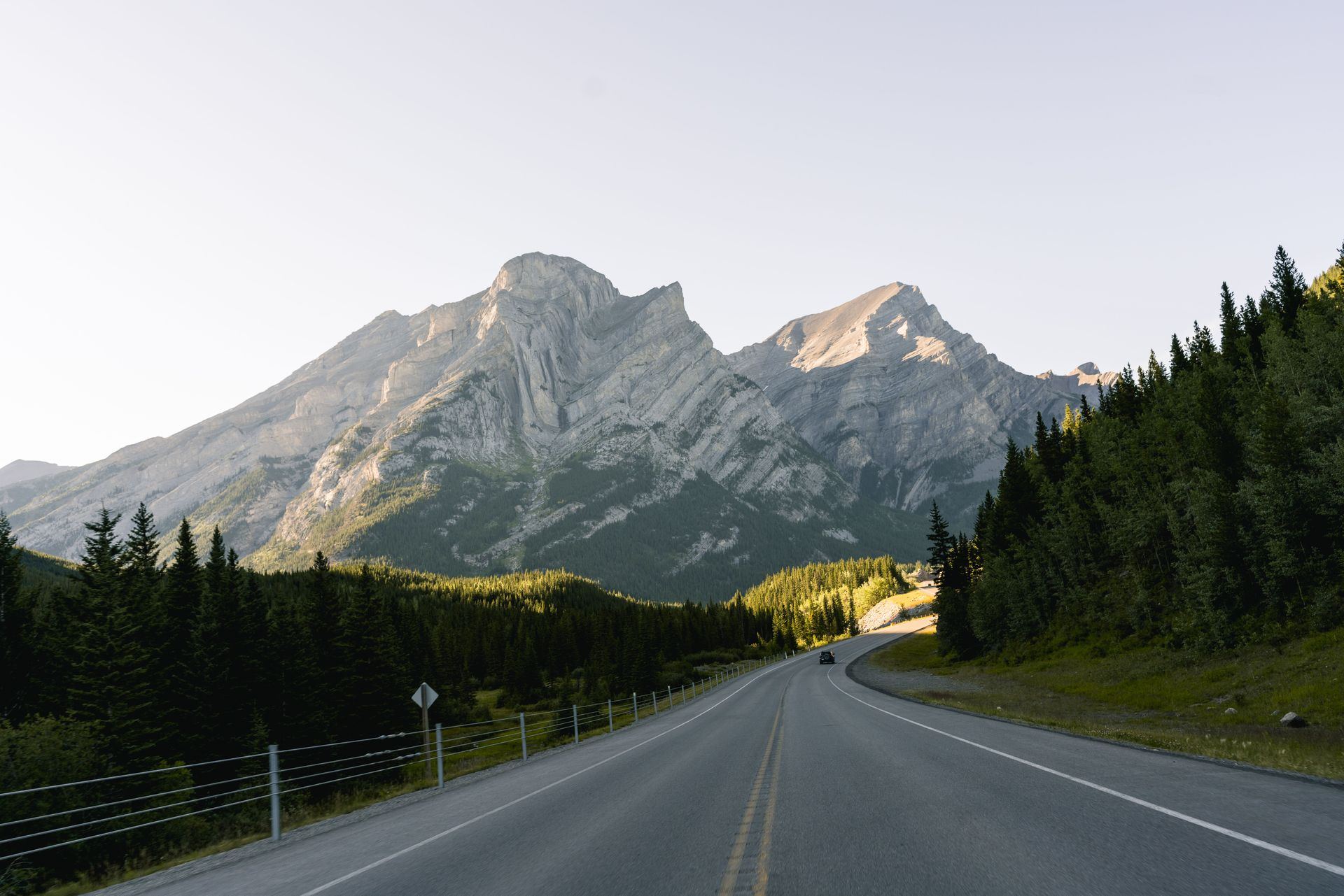 Een bergweg die bij zonsopgang in Banff National Park naar grillige bergtoppen leidt, met aan beide zijden dennenbomen.