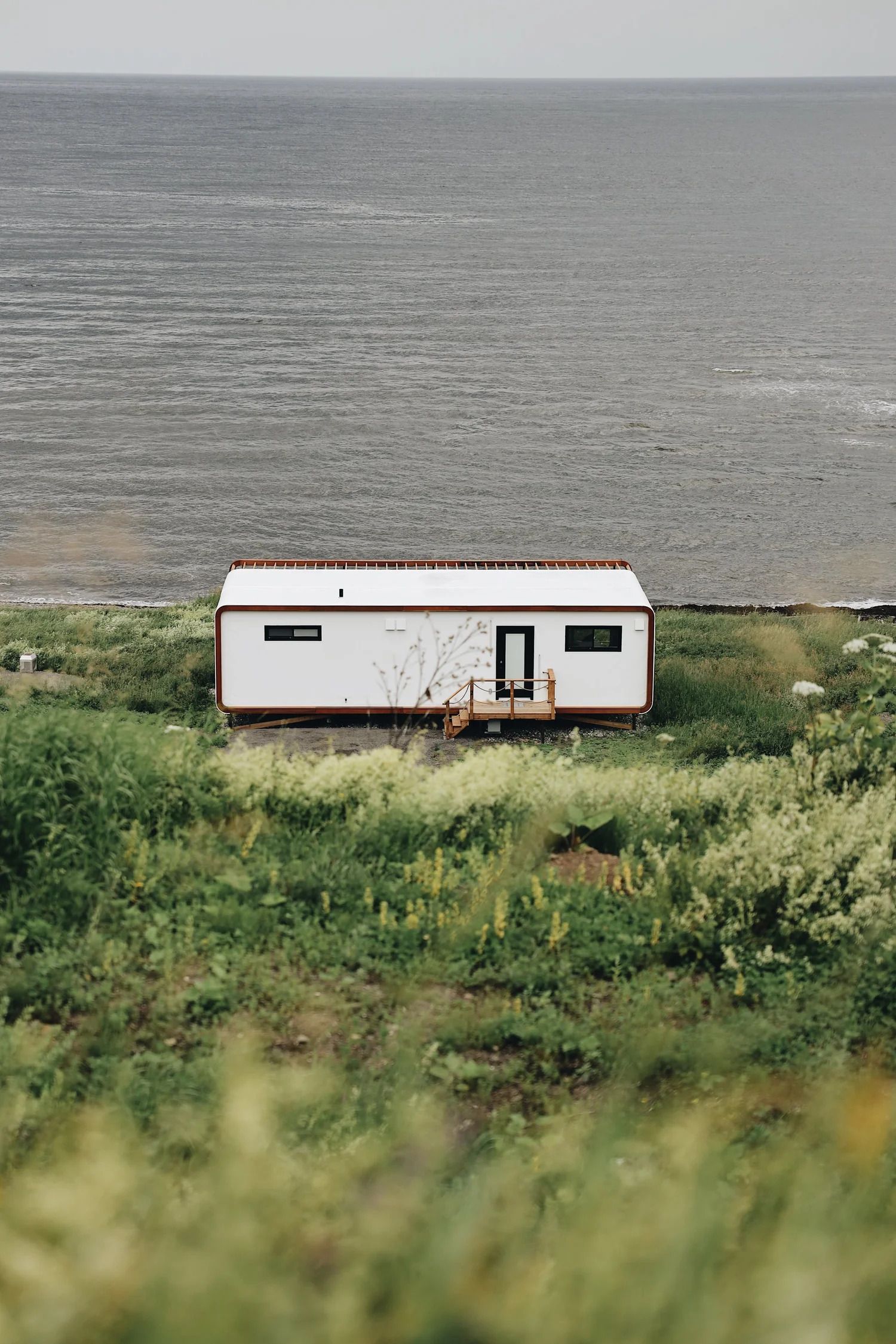 Witte caravan in een grasveld met een groot grijs wateroppervlak op de achtergrond.