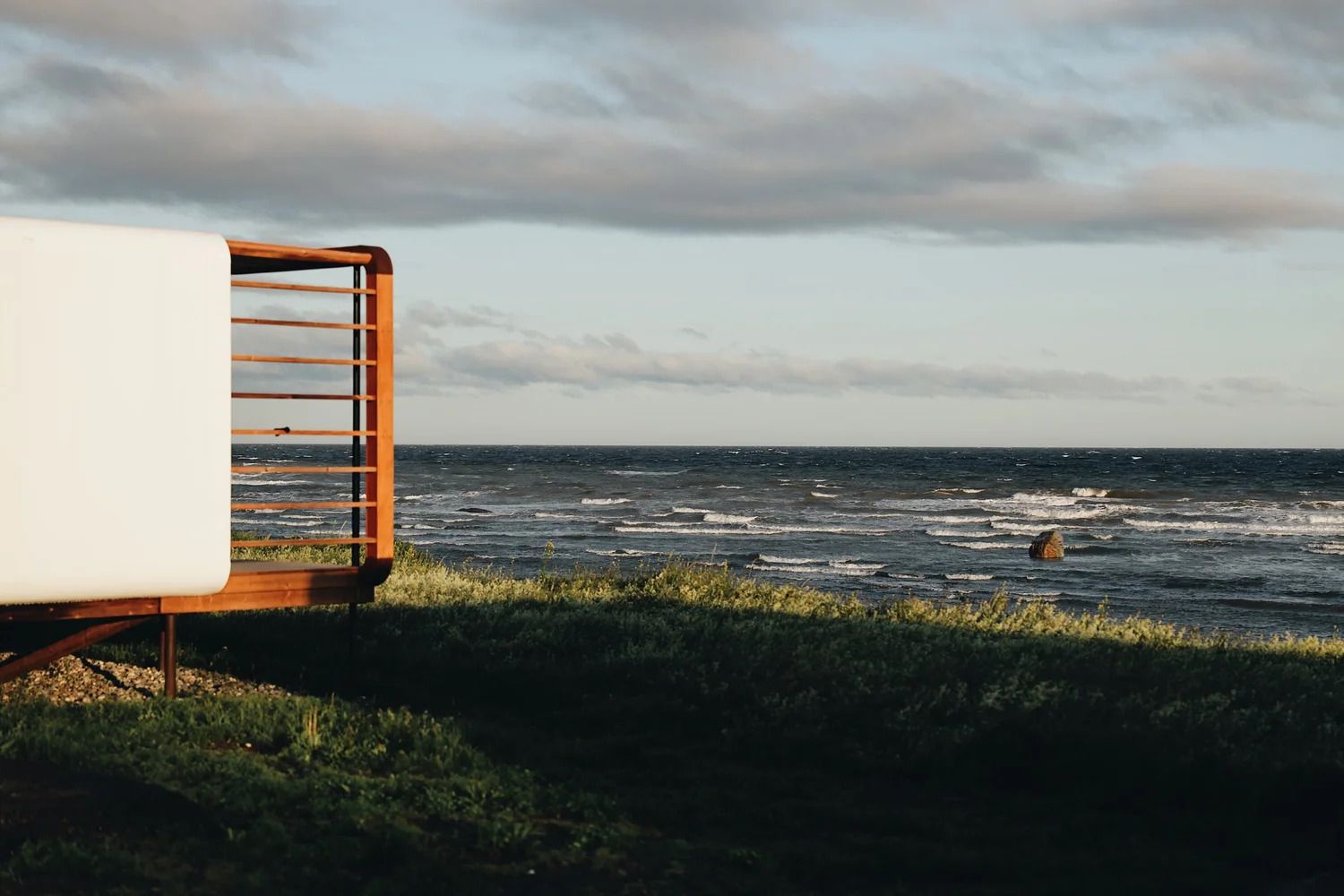 Uitzicht op zee met woelig water, bewolkte lucht en een wit gebouw aan de linkerkant.
