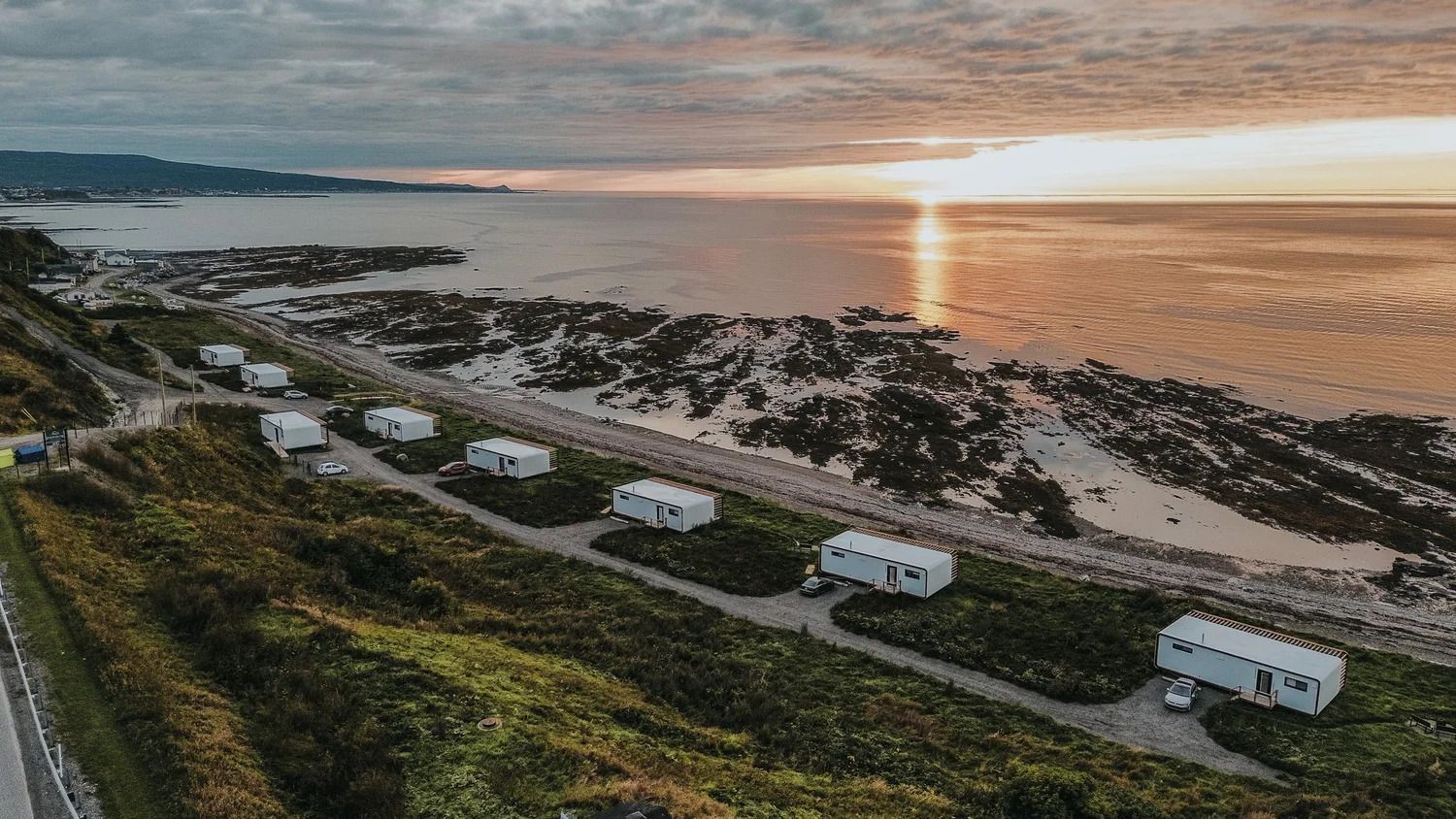 Campers staan geparkeerd langs een kustweg bij zonsondergang, met uitzicht op de oceaan.