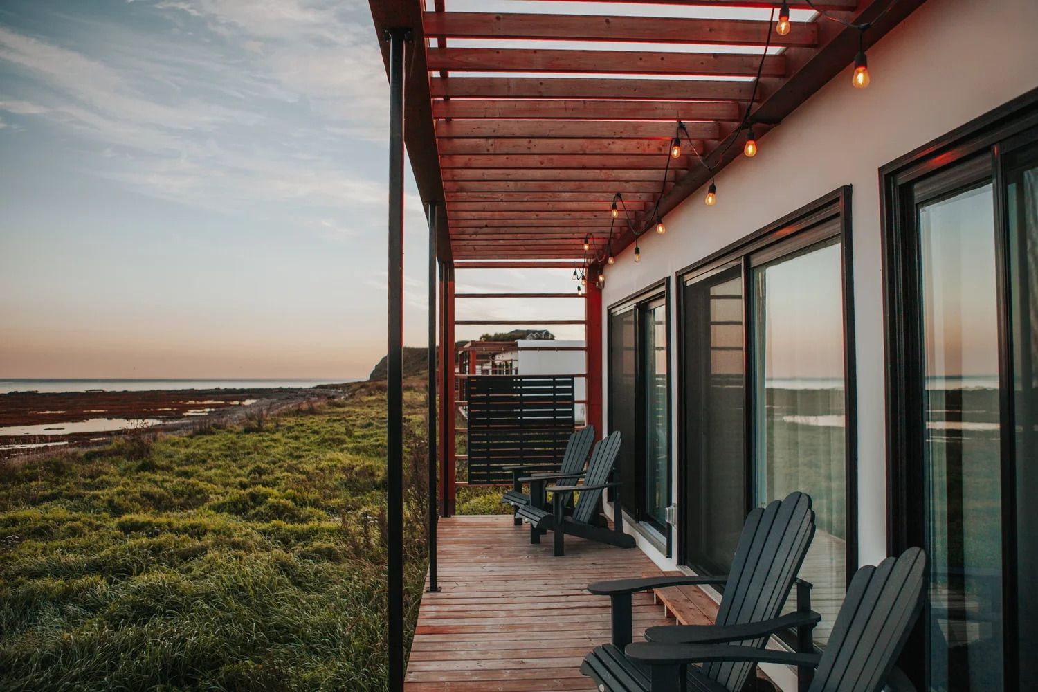 Houten terras van een strandhut met stoelen, glazen deuren en uitzicht op de zonsondergang boven het moerasland.