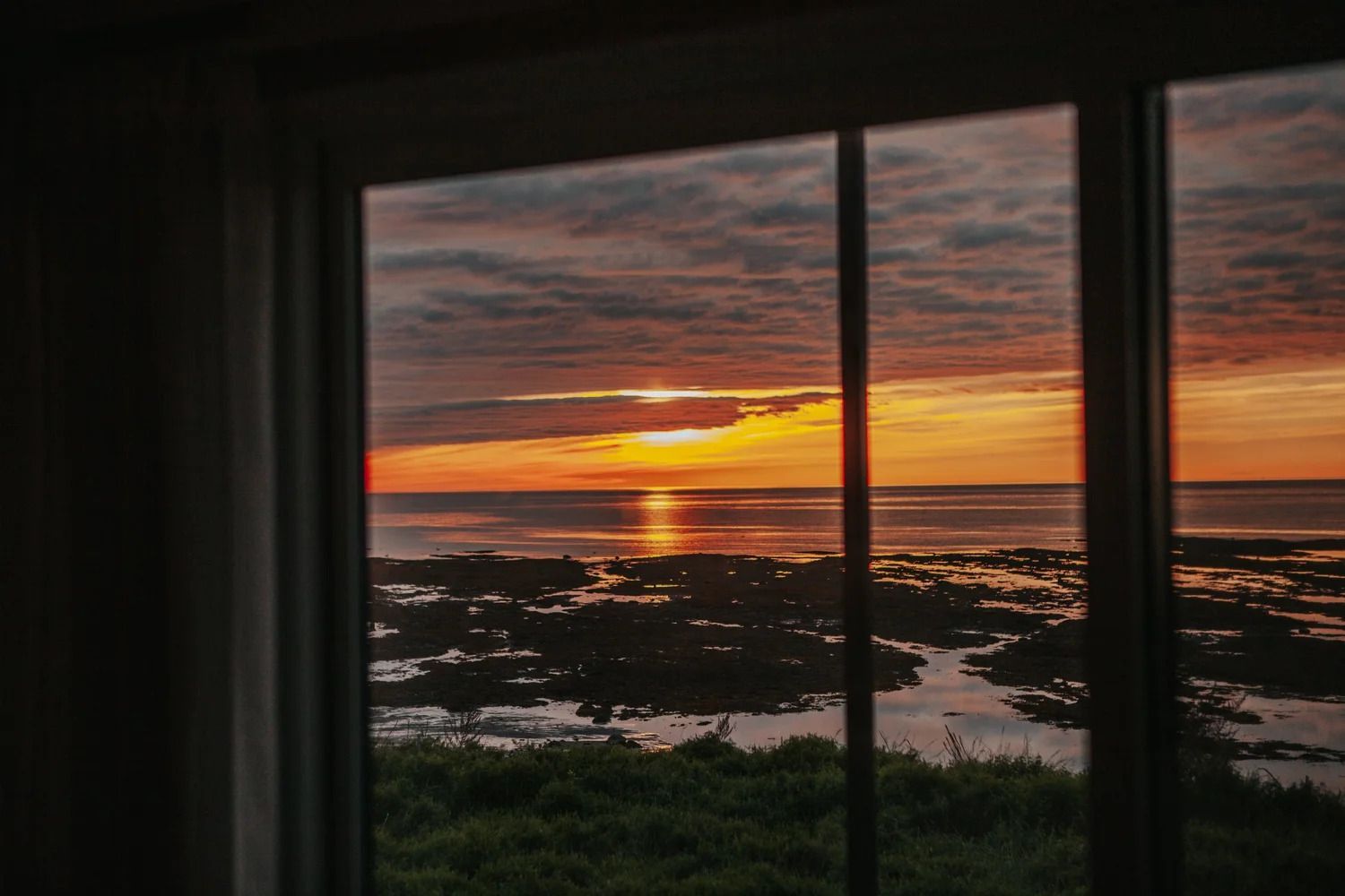 Zonsondergang boven een kalm wateroppervlak, gezien door donkere raamkozijnen, met een oranje en roze lucht.