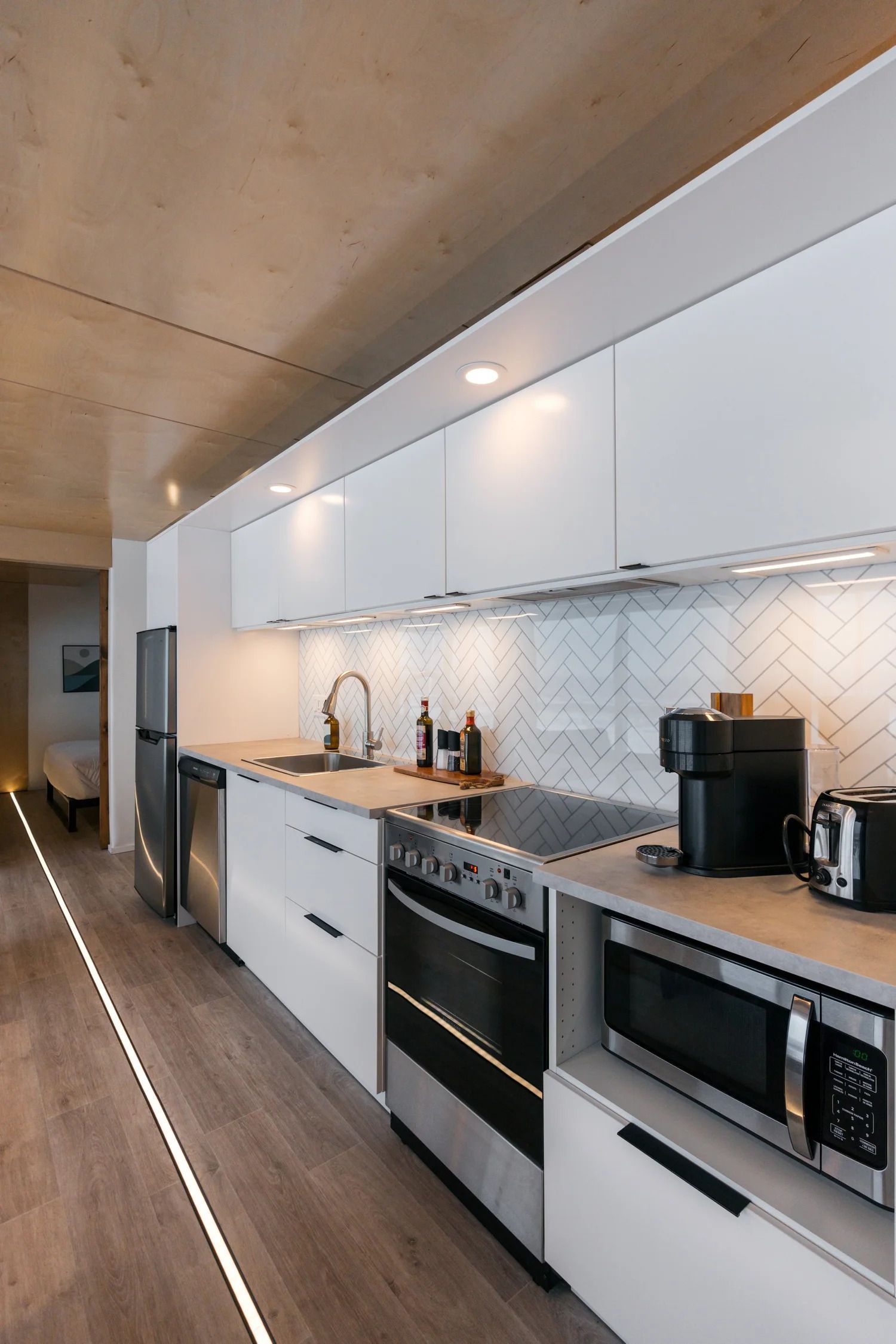 Moderne keuken met witte kasten, zwarte apparaten en een houten plafond in een smal appartement.