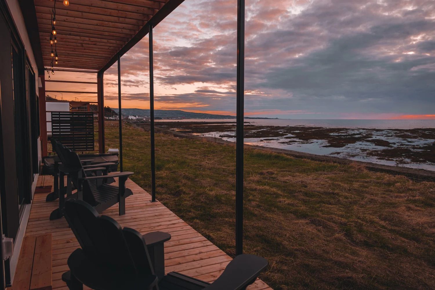 Veranda met uitzicht op een rotsachtige kustlijn bij zonsondergang, met roze wolken en kalm water.