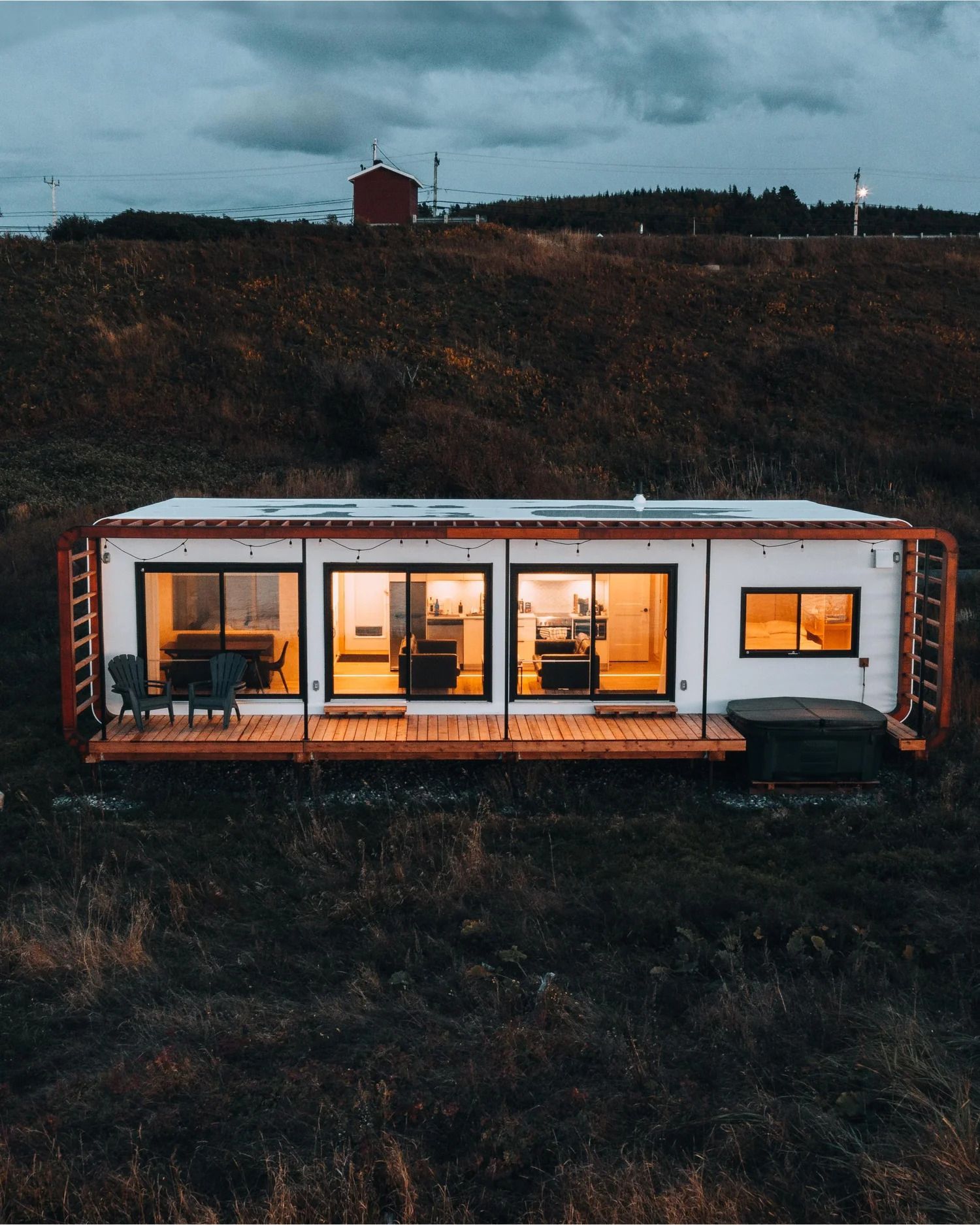 Modern wit tiny house met verlichte ramen op een donkere heuvel in de schemering