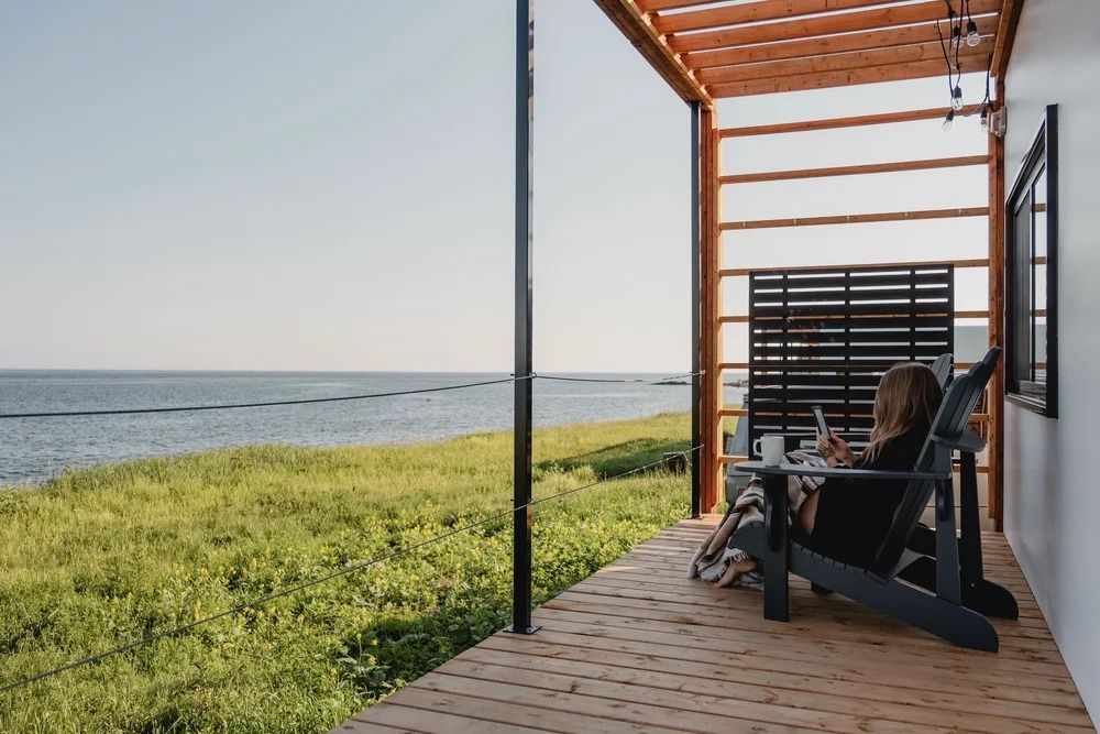 Overdekte veranda aan zee met een schommelstoel en uitzicht op de oceaan en het groene gras.