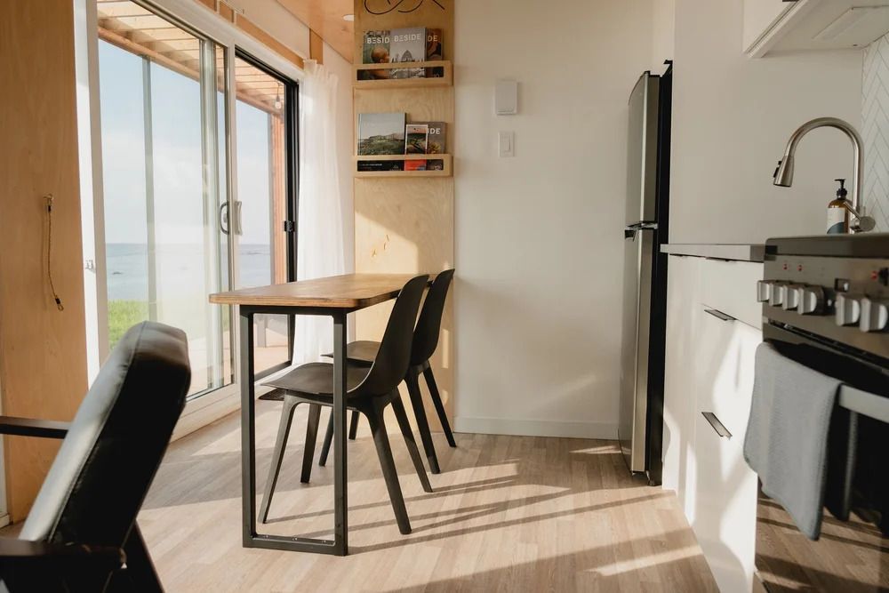 Lichte keuken en eethoek met houten tafel, zwarte stoelen en zonlicht op de vloer.