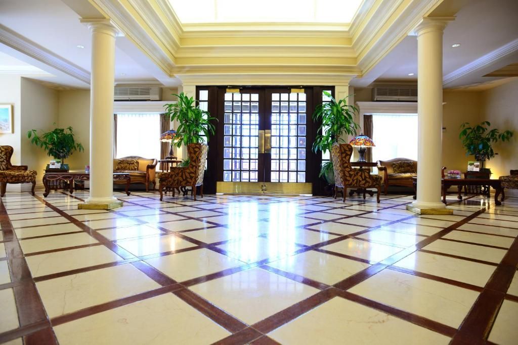 Elegante hotellobby met marmeren vloer, hoge zuilen, potplanten en grote ramen.