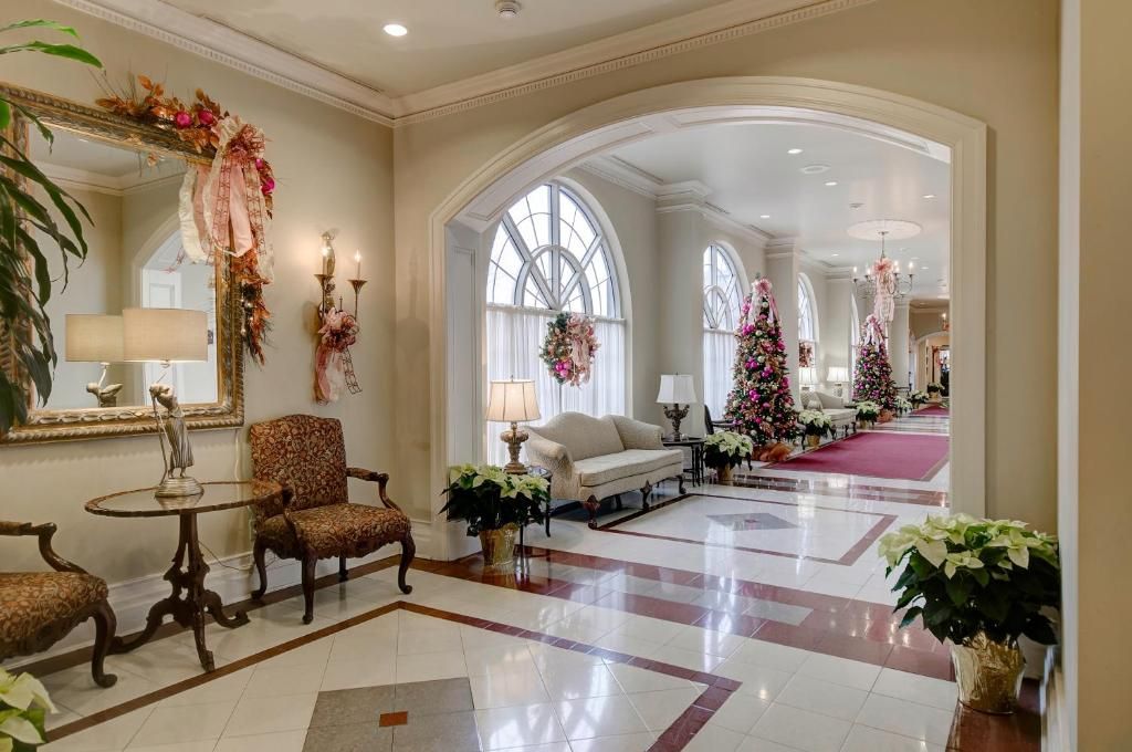Elegante hotellobby met marmeren vloeren, crèmekleurige muren, kroonluchters en bloemstukken.