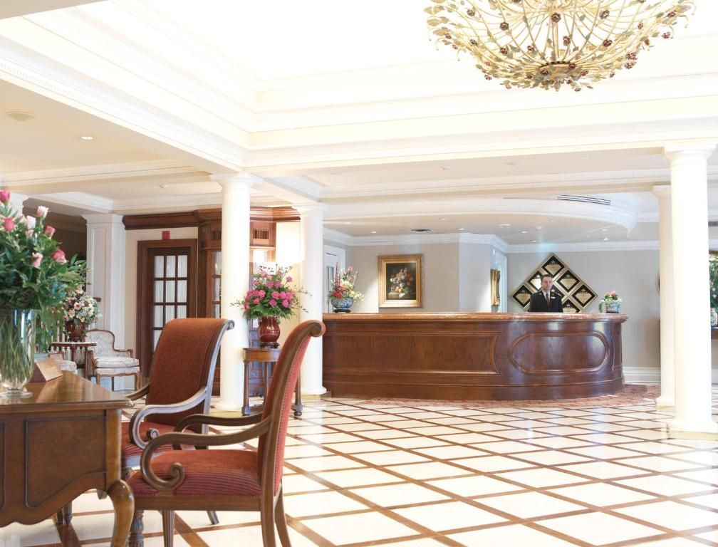 Lichte hotellobby met marmeren vloer, houten receptiebalie, zuilen, kroonluchter en zithoek.