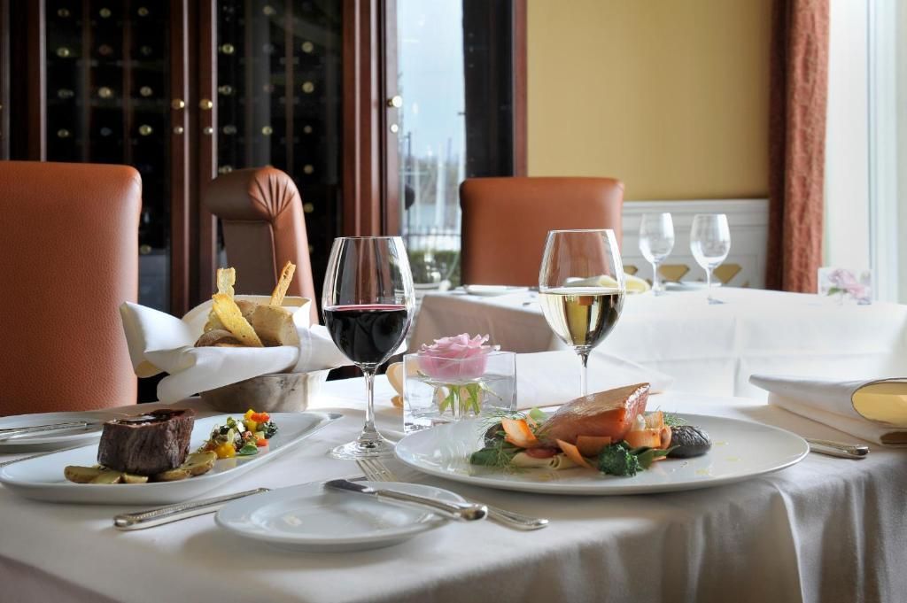 Een elegant gedekte restauranttafel bij een raam, met wijnglazen, borden met eten en witte tafelkleden.