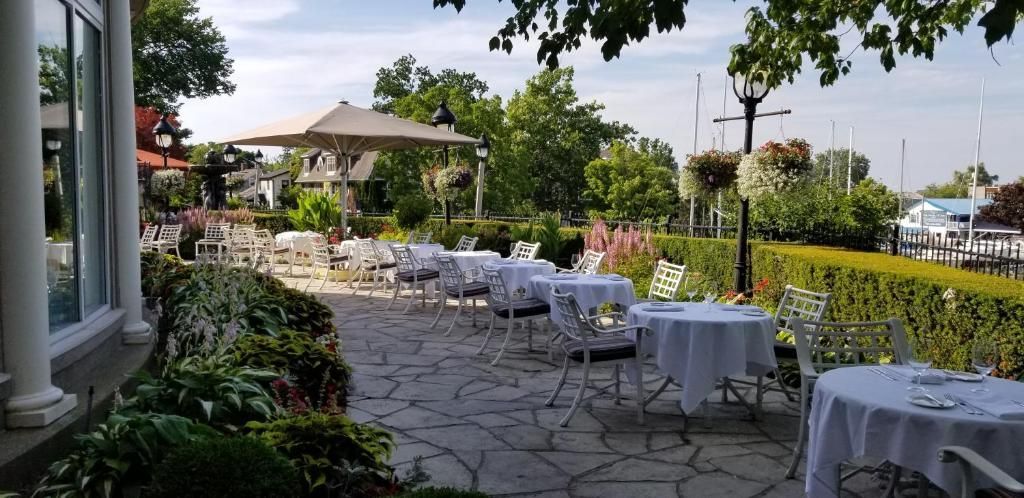 Buitenpatio met witte tafeldekking, hagen en uitzicht op een tuin naast een gebouw.