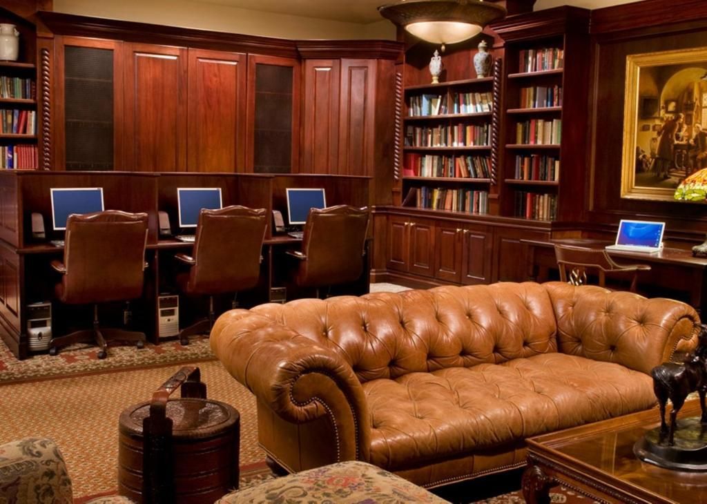 Bibliotheeklounge met houten lambrisering, leren bank, bureaus, stoelen en boekenkasten.