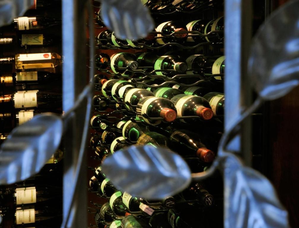 Wijnflessen opgeslagen in een wijnrek met glazen voorkant, met wazige bladeren op de voorgrond.