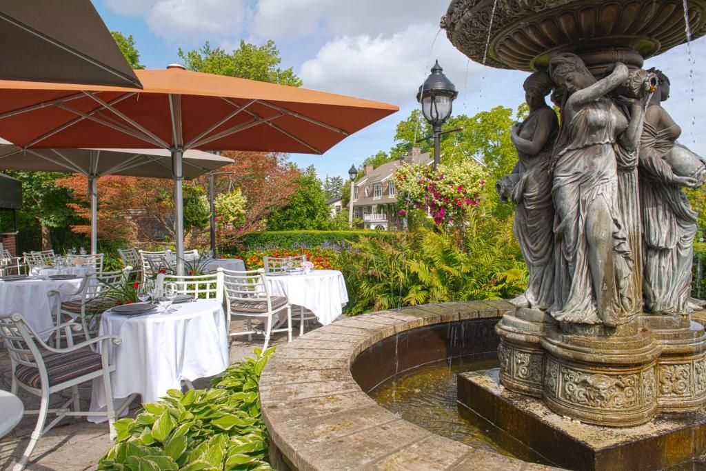 Eetgedeelte op het terras met witte tafels, oranje parasols en een stenen fontein op de voorgrond.