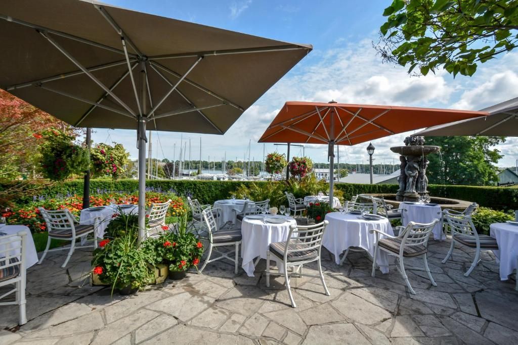 Een terras van een café in de buitenlucht met witte tafels en stoelen onder grote parasols, met uitzicht op het water.