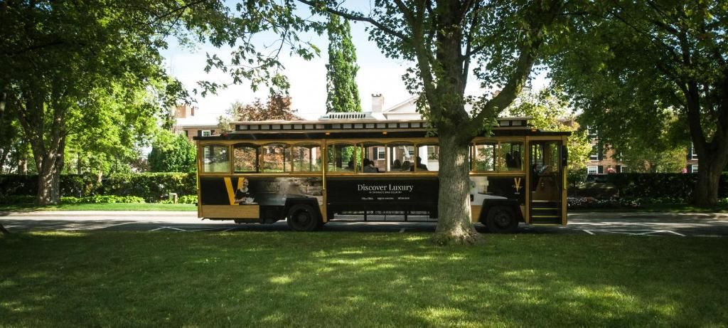 Gele trolleybus geparkeerd onder bomen in een grasrijk park.