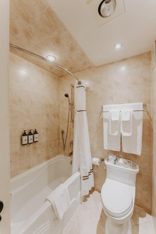 Kleine beige badkamer met bad, douche, toilet, wastafel en witte handdoeken.