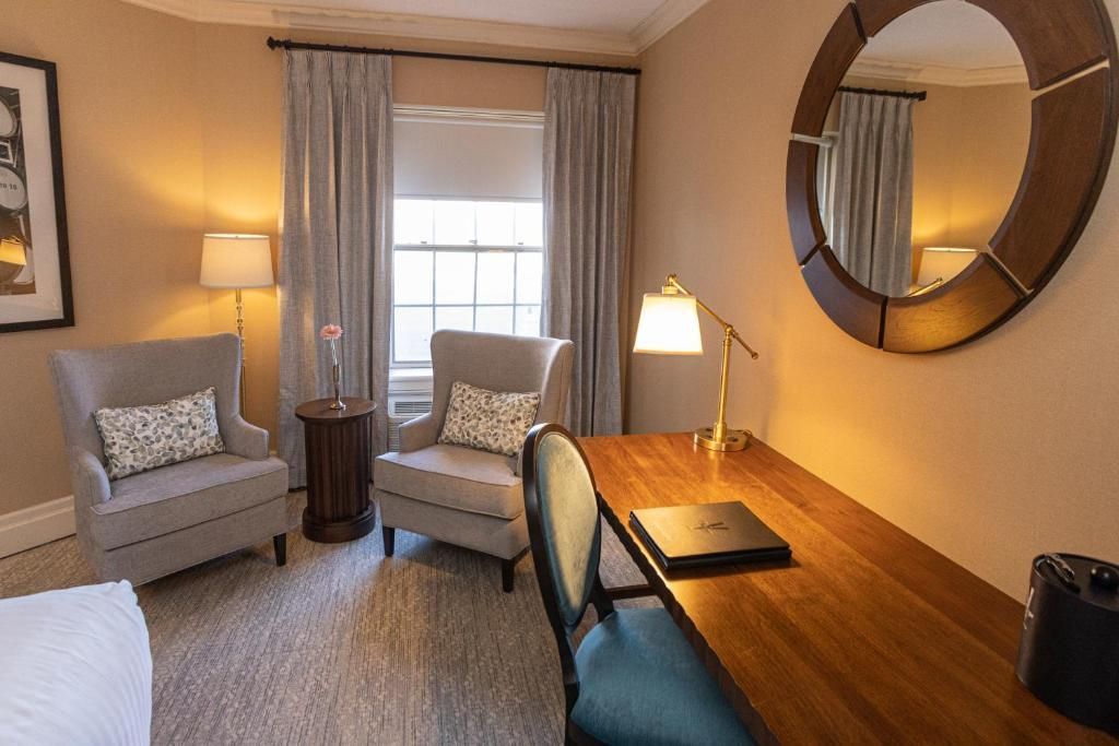Gezellige thuiswerkplek met bureau, turquoise stoel, fauteuil, lamp en grote ronde spiegel in een beige kamer.