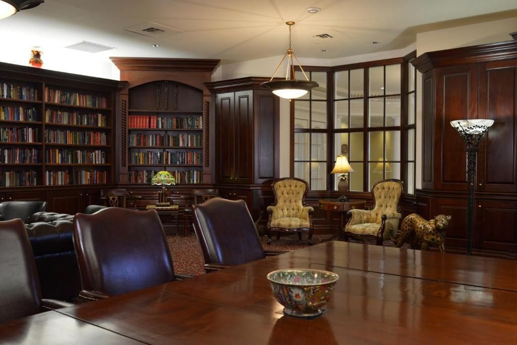 Formele vergaderruimte in de bibliotheek met houten tafel, leren stoelen, boekenkasten en sfeervolle verlichting.