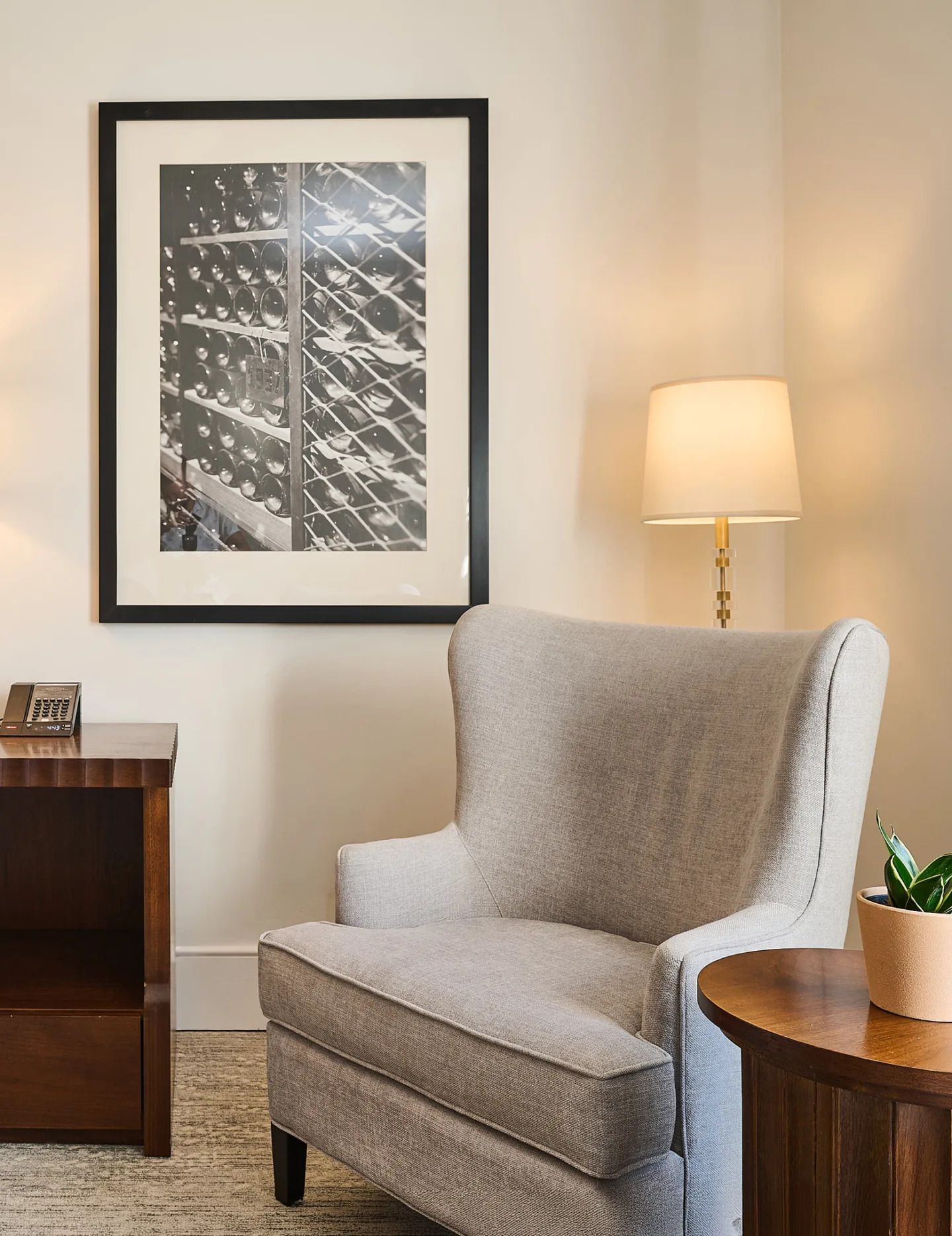 Gezellige zithoek in de woonkamer met een grijze fauteuil, staande lamp, ingelijste kunst aan de muur en een houten bijzettafel.