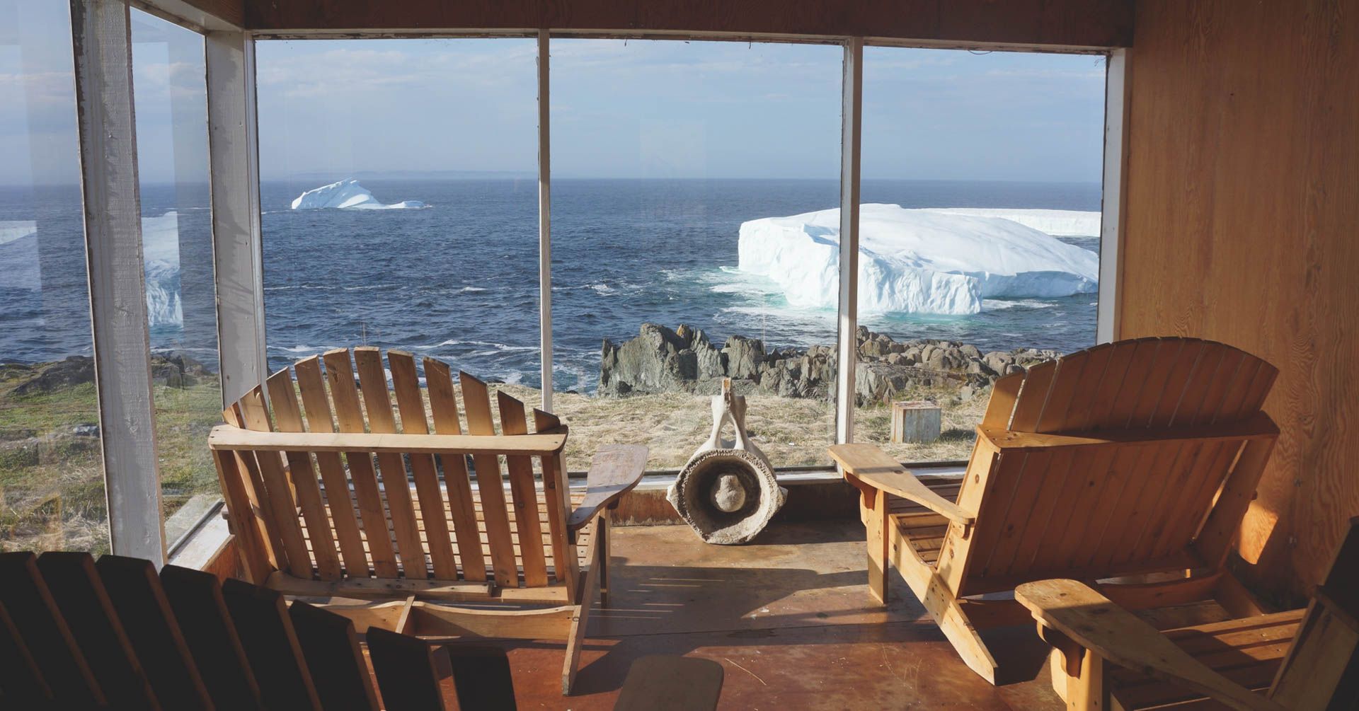 Houten stoelen op een veranda met uitzicht op de oceaan en de verre ijsbergen door grote ramen.