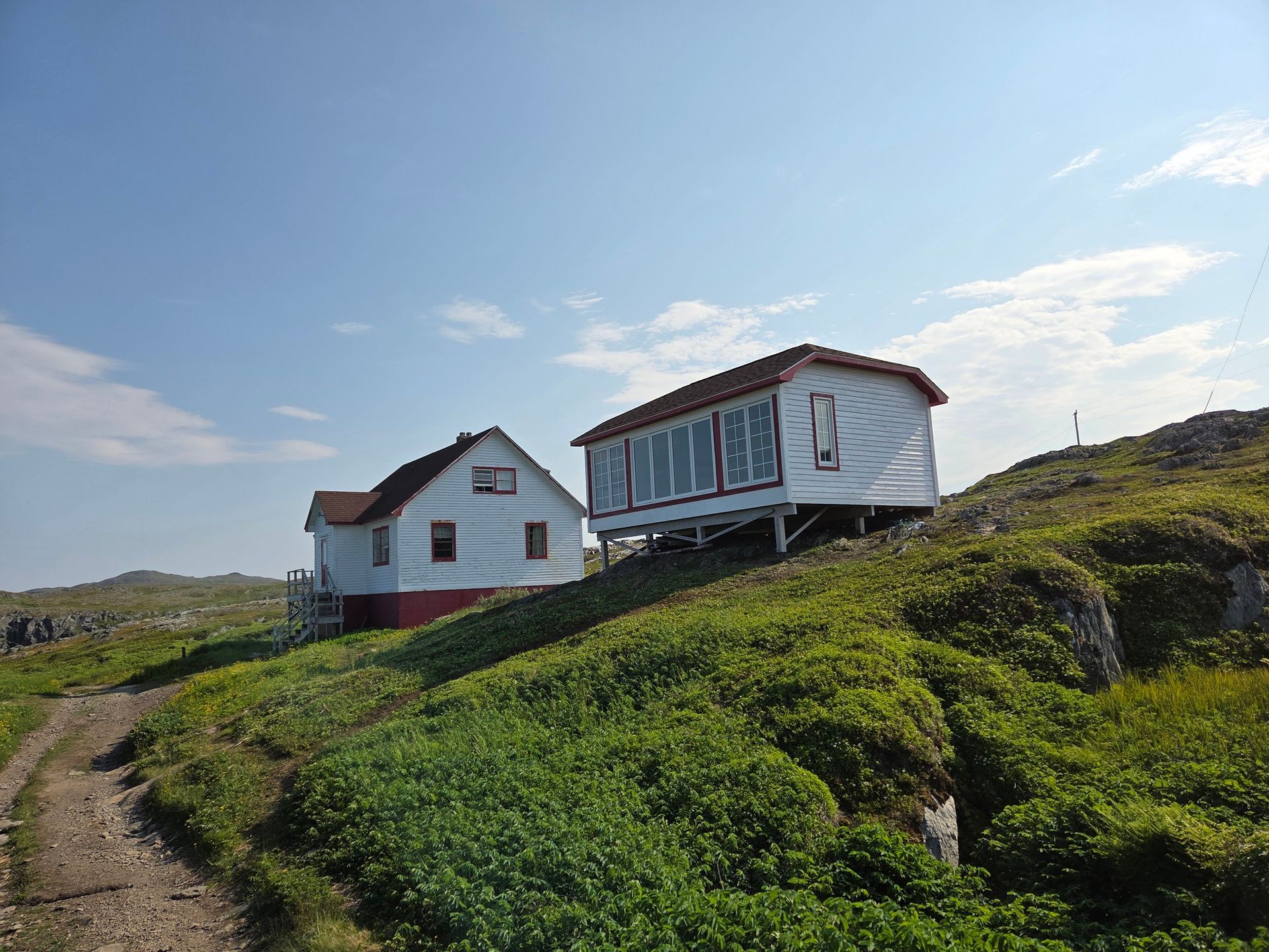 Twee witte huizen van Quirpon Lighthouse Inn op een grashelling onder een blauwe hemel.