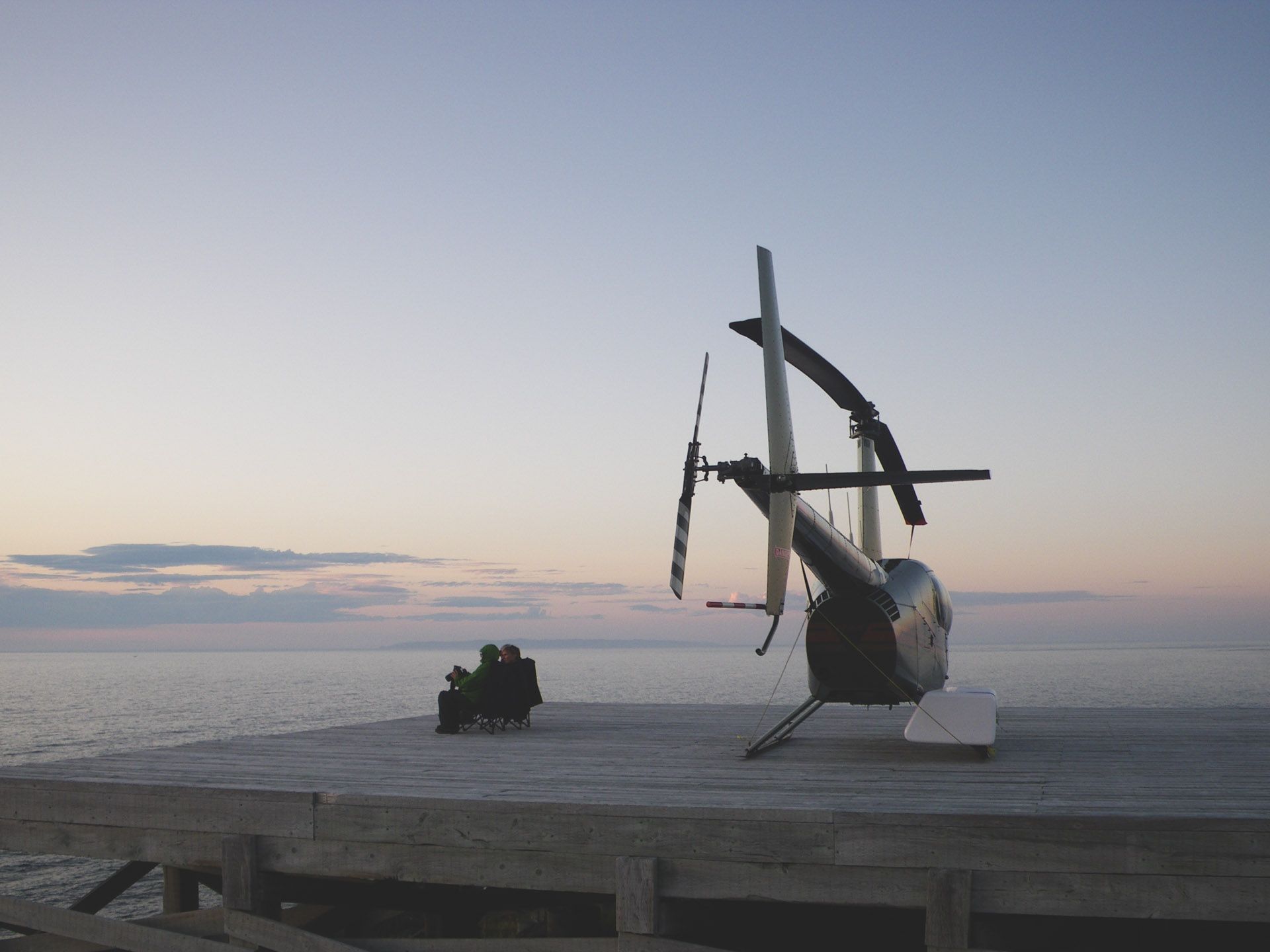 Helikopter op een besneeuwde vlakte in de schemering, met een klein voertuig ernaast onder een bleke hemel.