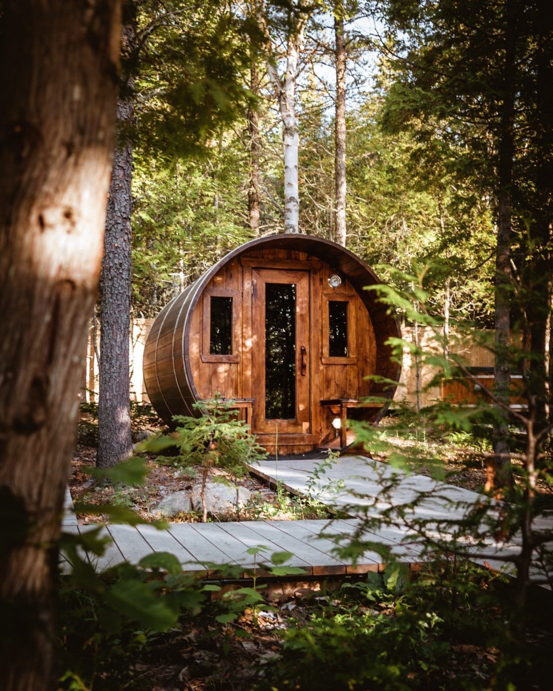 Een kleine, ronde houten hut in een bos, omgeven door een stenen pad en bomen.